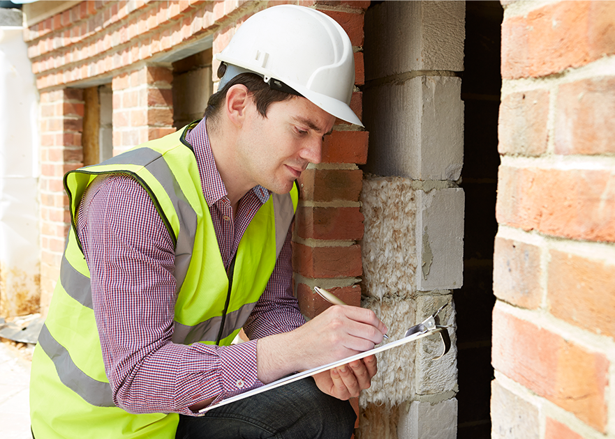 man in high vis and safety helmet assessing a building and making notes