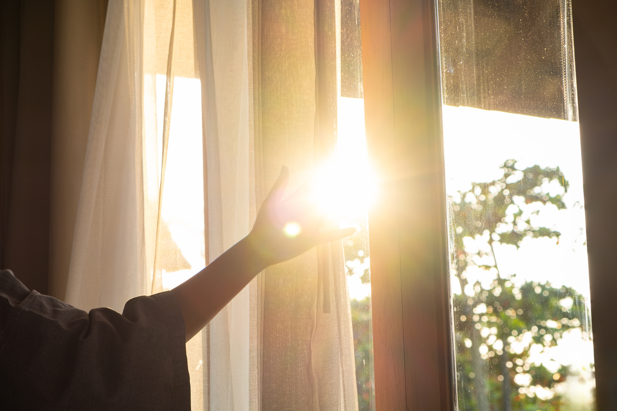 A woman's hand opening the curtains. Sun is beaming in through the window